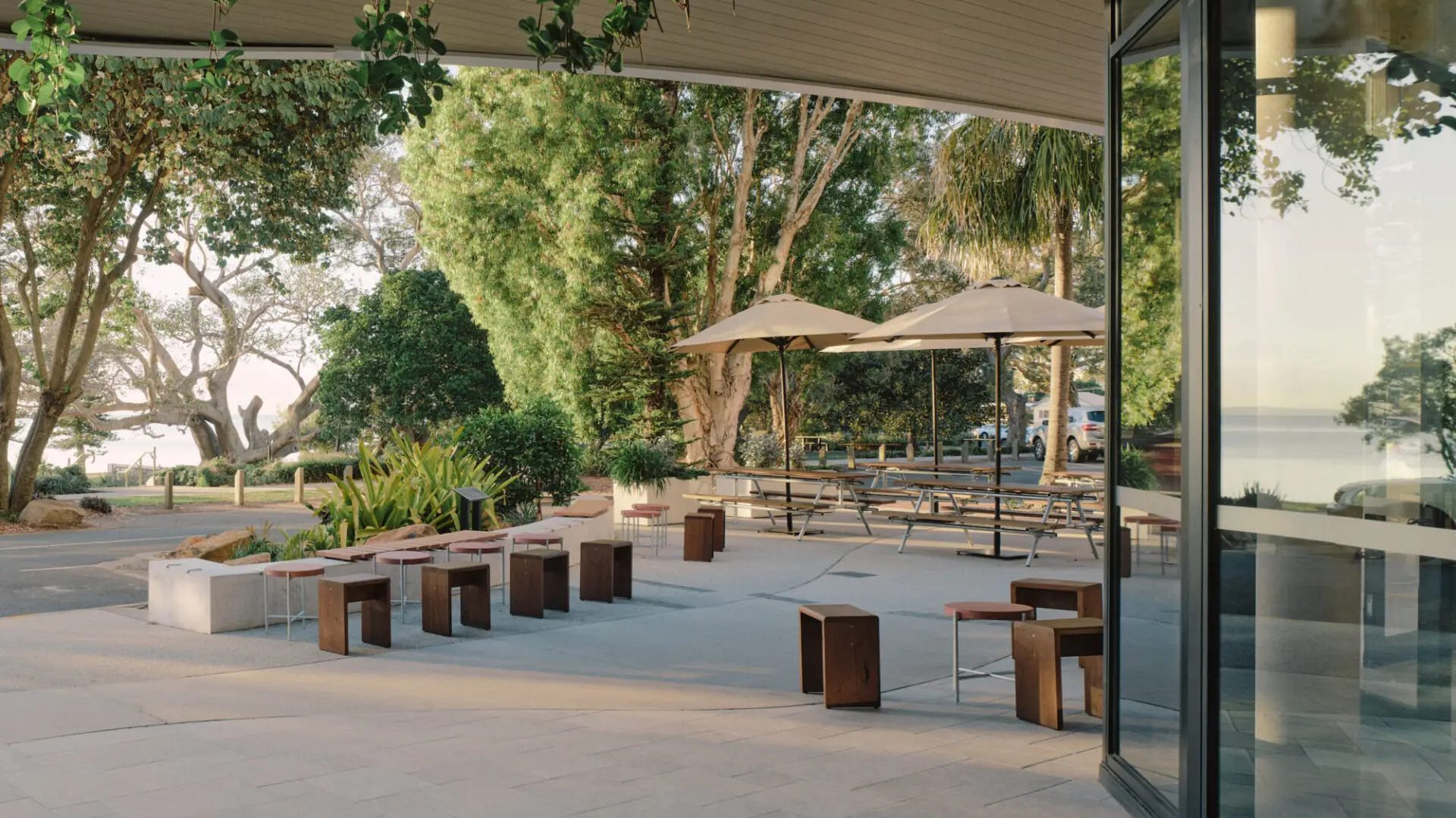 Warm timber communal tables and pigmented sand-cast concrete furnishings define the coastal-inspired hospitality space that achieved 84% embodied carbon reduction.
